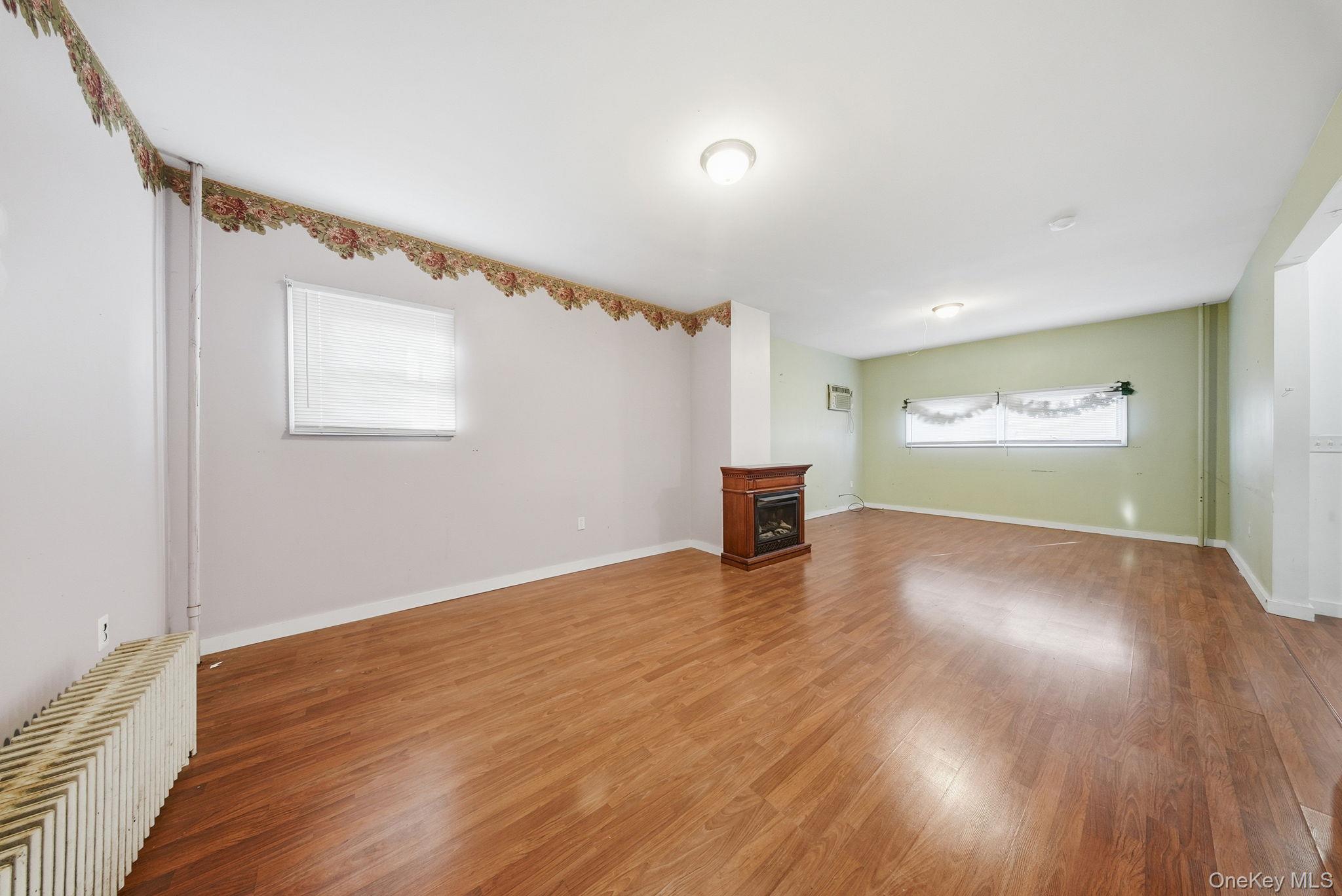 21 Ridge Street Middletown, NY 10940 - Photo 10 of 32 Unfurnished living room with wood finished floors, a fireplace, radiator heating unit, and a wall unit AC