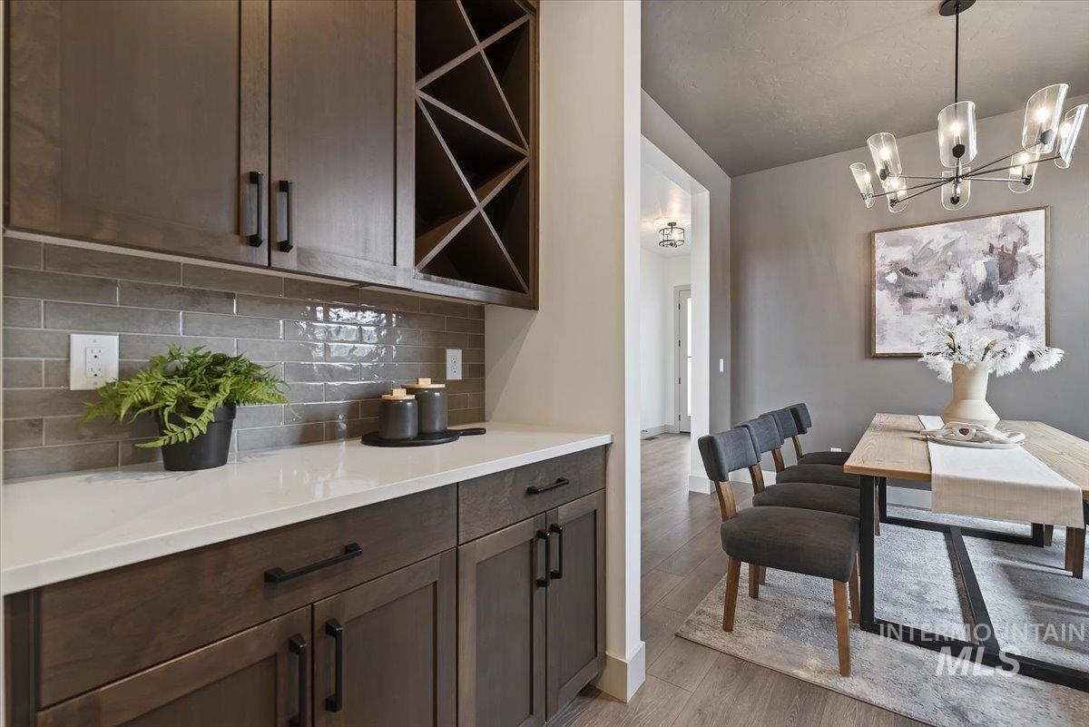 8458 West Graye Street, Unit RAINIER Meridian, ID 83646 - Photo 6 of 29 Bar with dark wood finish cabinets, light wood-type flooring, decorative backsplash, suspended lighting, and open shelves