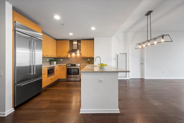 a kitchen with stainless steel appliances granite countertop a refrigerator a sink a stove and oven with wooden floor