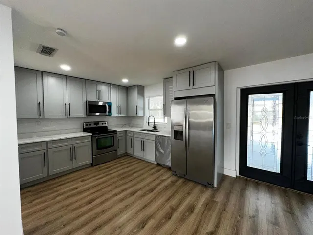 a kitchen with stainless steel appliances granite countertop a refrigerator a sink dishwasher a stove and a refrigerator with wooden floor