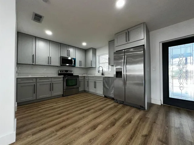 a kitchen with stainless steel appliances granite countertop a stove a sink dishwasher a refrigerator and a microwave oven with wooden floor