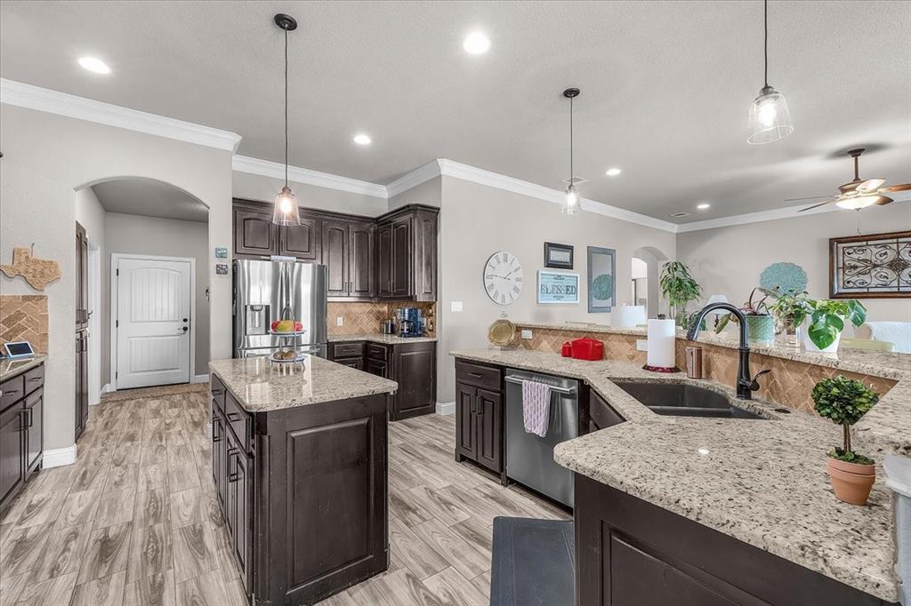 139 Stanford Lane Springtown, TX 76082 - Photo 13 of 36 Kitchen featuring arched walkways, dark wood finish cabinets, a center island, backsplash, and ornamental molding
