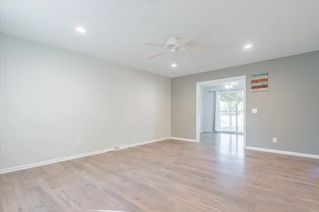 a view of an empty room with wooden floor and a ceiling fan