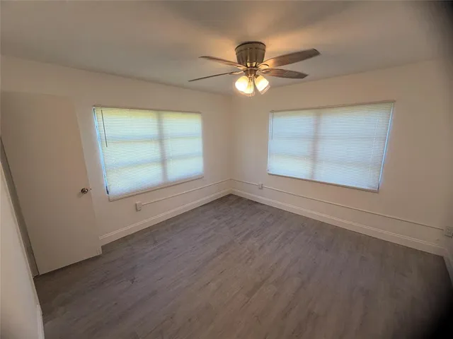 an empty room with wooden floor fan and windows