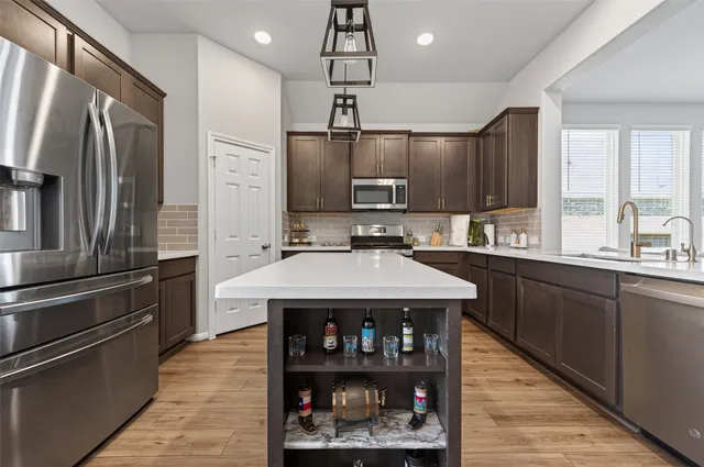 a kitchen with stainless steel appliances granite countertop a stove a sink dishwasher a refrigerator and a dining table with wooden floor