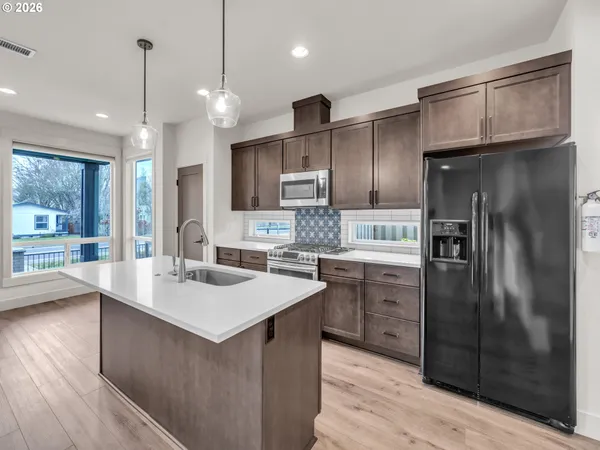a kitchen with stainless steel appliances granite countertop a refrigerator a sink dishwasher a stove and white cabinets with wooden floor