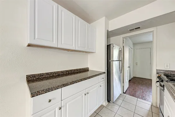 a kitchen with granite countertop a refrigerator and white cabinets