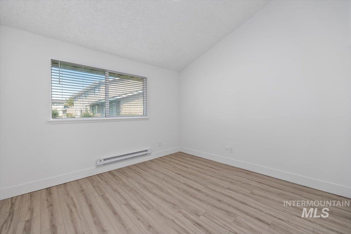 259 Pheasant Road West, Unit 3 Twin Falls, ID 83301 - Photo 11 of 24 Empty room with a textured ceiling, vaulted ceiling, a baseboard radiator, and light wood-style flooring