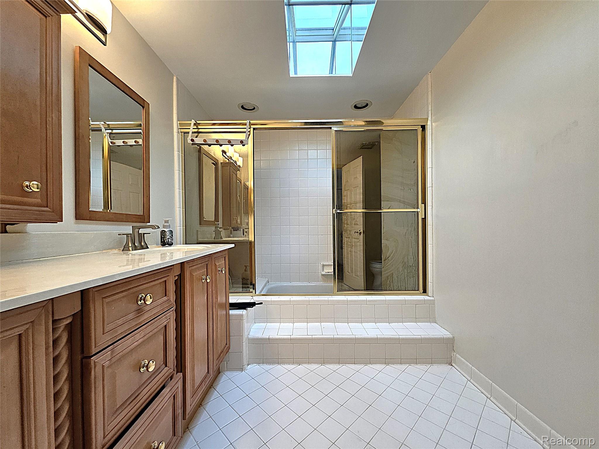 1114 Chaffer Drive Rochester, MI 48306 - Photo 40 of 50 Bathroom featuring a skylight, wood-finish vanity with a light-toned countertop, framed mirror, and a shower enclosure with sliding glass doors