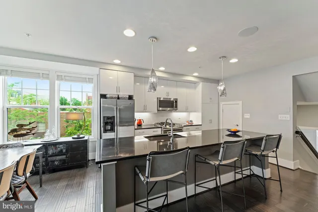 a kitchen with stainless steel appliances granite countertop a stove top oven a refrigerator a sink dishwasher a dining table and chairs with wooden floor