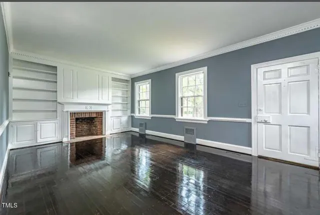 an empty room with wooden floor fireplace and windows