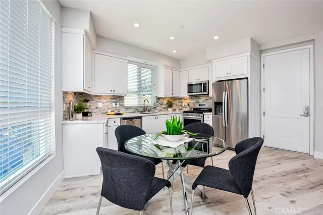 a kitchen with stainless steel appliances granite countertop a dining table chairs refrigerator and a window