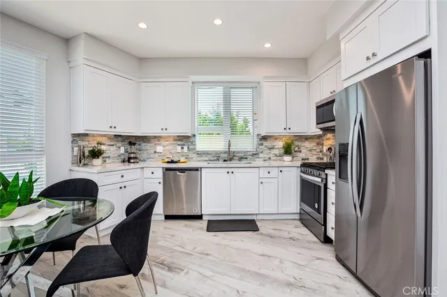 a kitchen with a refrigerator a stove a sink dishwasher a dining table and chairs with wooden floor