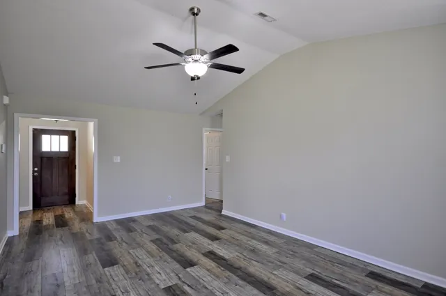an empty room with wooden floor fan and windows