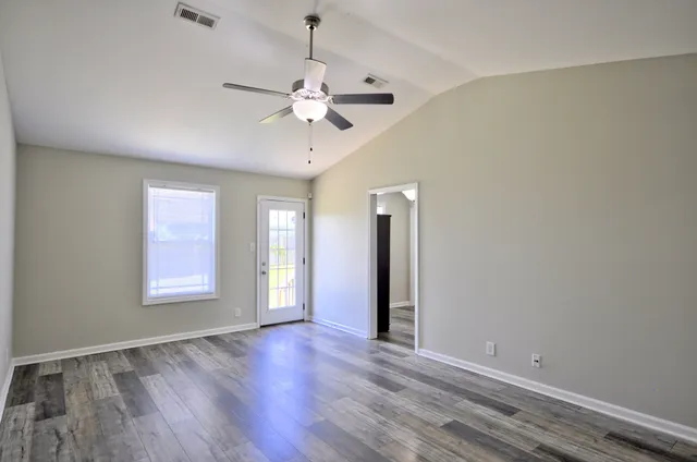 an empty room with wooden floor chandelier fan and windows