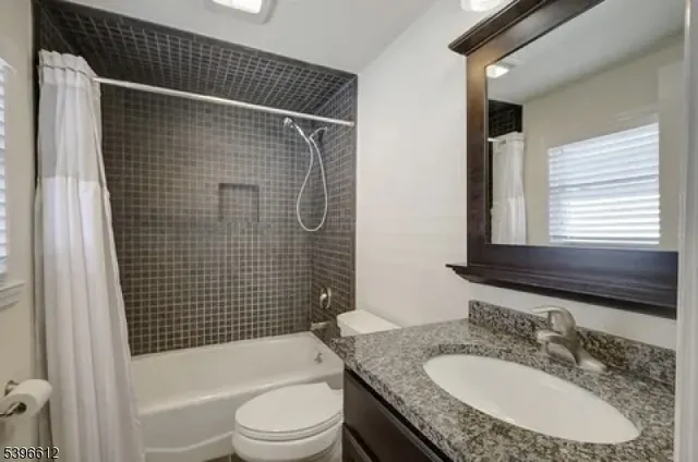 a bathroom with a granite countertop bathtub sink vanity mirror and toilet