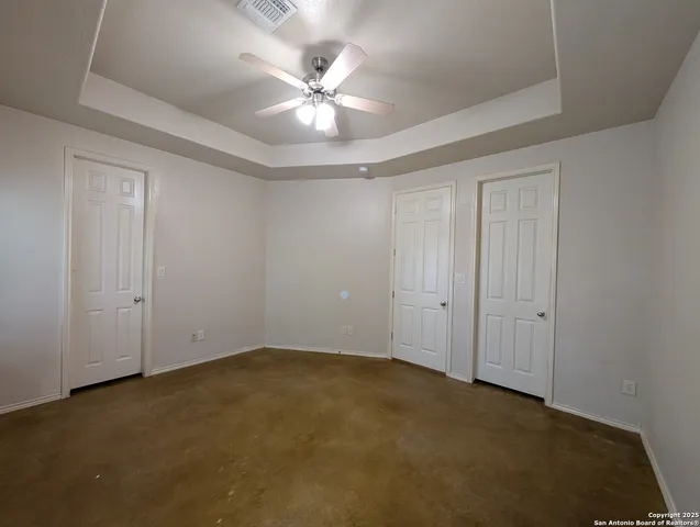an empty room with a chandelier fan and wooden floor
