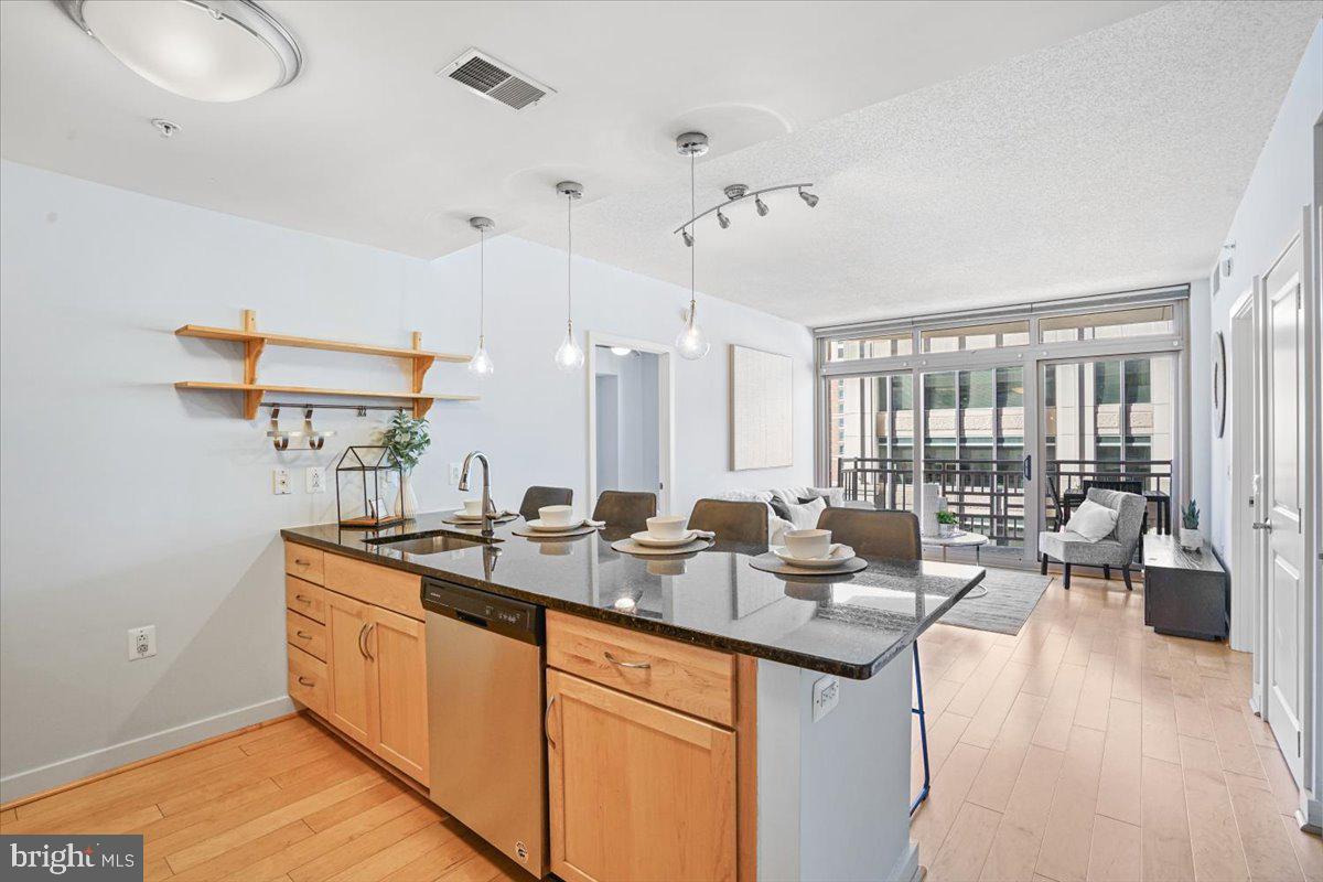 a open kitchen with stainless steel appliances granite countertop a sink dishwasher and a flat tv screen next to a large window with wooden floor