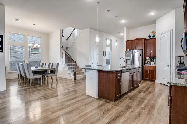 a kitchen with stainless steel appliances kitchen island granite countertop a refrigerator a stove top oven and a dining table with wooden floor