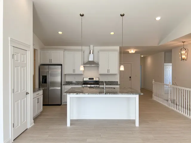 a large kitchen with stainless steel appliances granite countertop a stove a sink a refrigerator and white cabinets with wooden floor