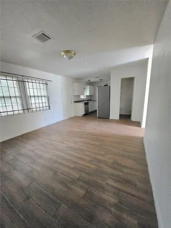 an empty room with wooden floor and kitchen view