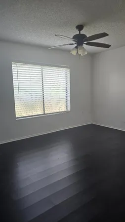 an empty room with wooden floor fan and windows