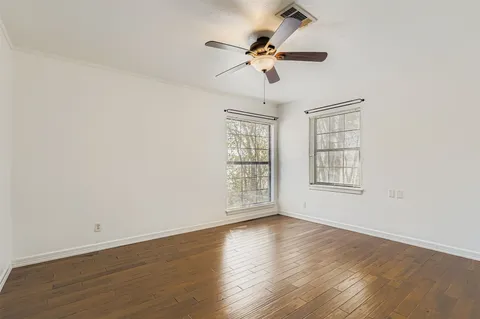 an empty room with wooden floor fan and windows