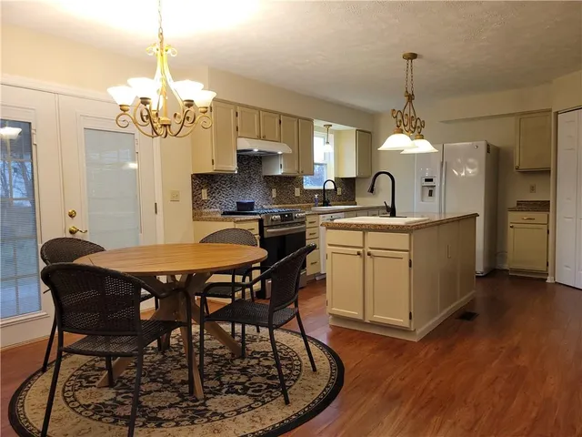 a kitchen with stainless steel appliances a dining table chairs a sink and dishwasher a refrigerator with wooden floor