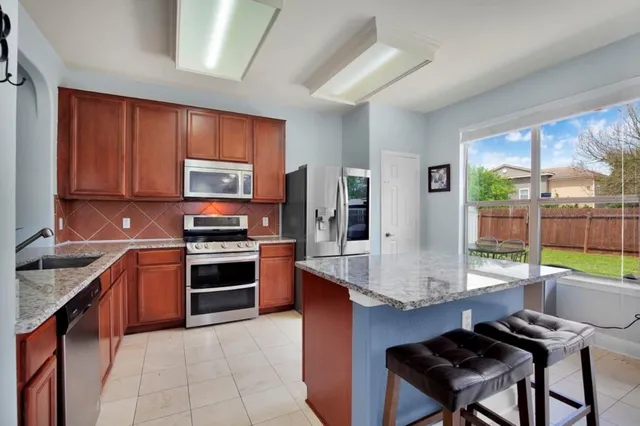 a kitchen with stainless steel appliances granite countertop a stove top oven a sink dishwasher a dining table and chairs with wooden floor