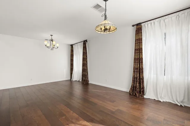 an empty room with wooden floor chandelier and windows
