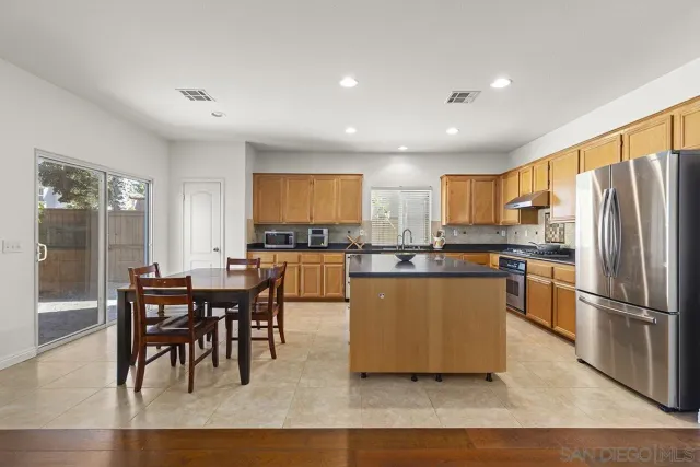 a kitchen with stainless steel appliances granite countertop a stove a sink a refrigerator a dining table and chairs