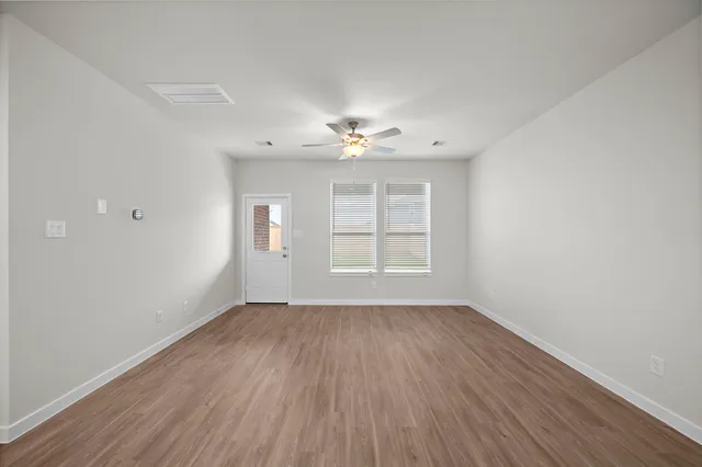 an empty room with wooden floor chandelier fan and windows