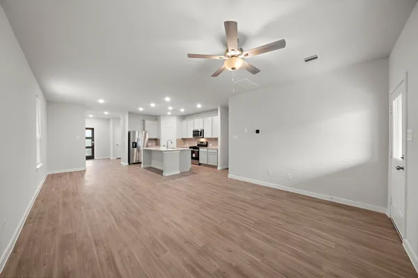 a view of an empty room with wooden floor and a ceiling fan