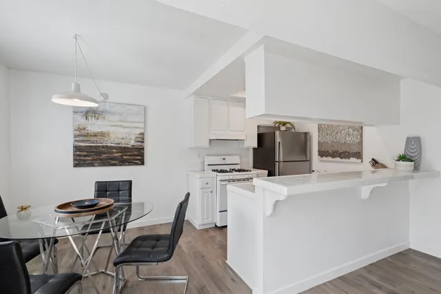 a kitchen with stainless steel appliances granite countertop a stove top oven a sink a refrigerator white cabinets and wooden floor