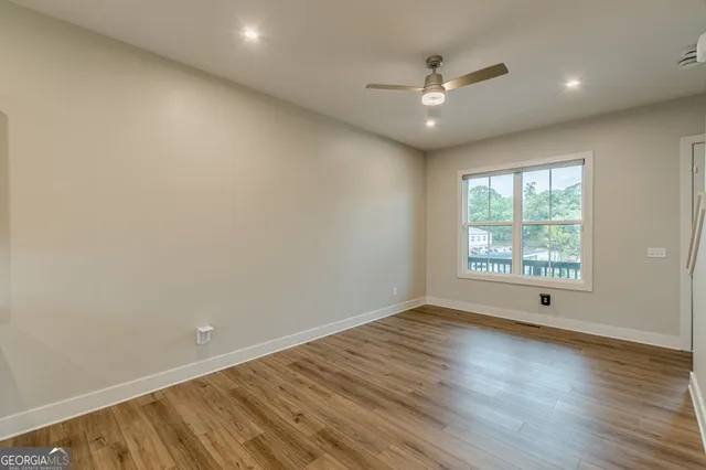 a view of an empty room with wooden floor and a kitchen