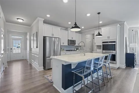 a kitchen with stainless steel appliances kitchen island granite countertop a refrigerator a sink dishwasher a stove a dining table and chairs with wooden floor