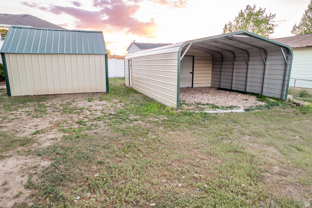 634 South 2100th Street West Vernal, UT 84078 - Photo 58 of 71 Expansive backyard featuring two metal storage structures: one fully enclosed with a green roof, and one open-sided carport with a gravel base and partial enclosure