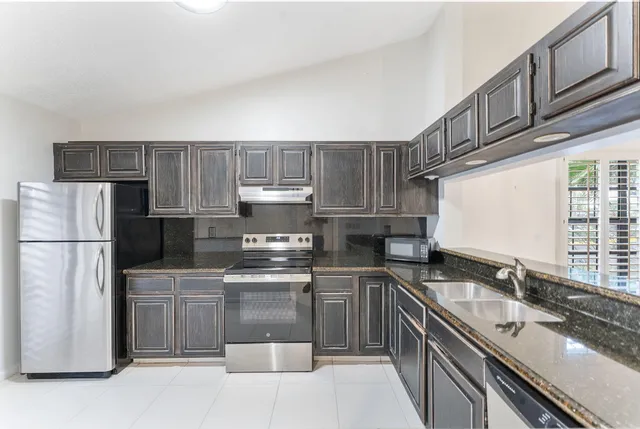 a kitchen with stainless steel appliances granite countertop a sink stove refrigerator and cabinets