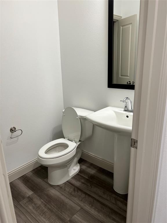6041 Roper Road McKinney, TX 75070 - Photo 8 of 24 Compact powder room featuring a pedestal sink with a chrome faucet, a white toilet, wood-finish flooring, and a framed mirror