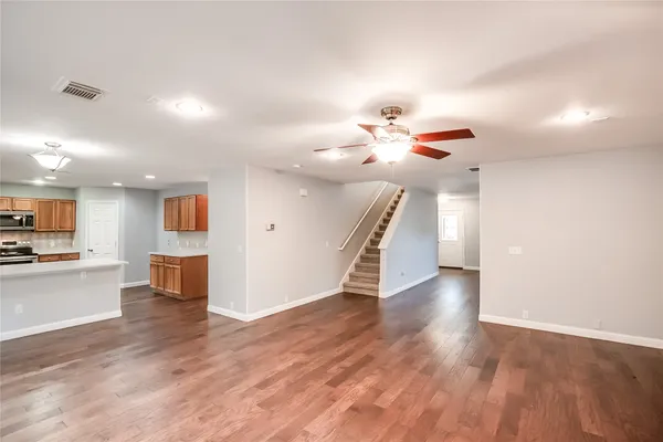 a view of an empty room with wooden floor and a kitchen