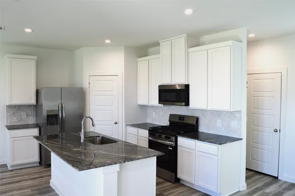 a kitchen with stainless steel appliances granite countertop a sink a stove a refrigerator a microwave a sink and white cabinets with wooden floor