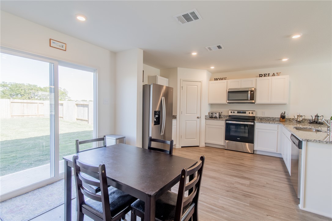 6029 Toby Bend Bryan, TX 77807 - Photo 8 of 25 a kitchen with stainless steel appliances granite countertop a stove a refrigerator a sink a dining table and chairs with wooden floor