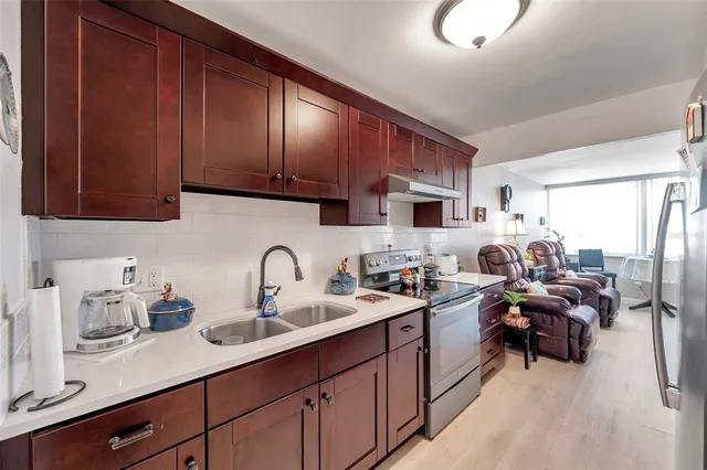 a kitchen with stainless steel appliances granite countertop a refrigerator a stove and a sink with living area