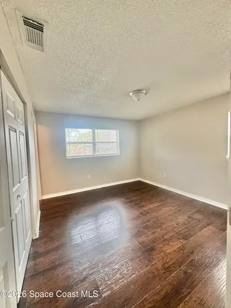 a view of an empty room with window and wooden floor