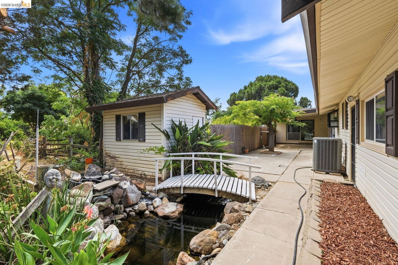 1590 Sunset Road Brentwood, CA 94513 - Photo 33 of 45 Backyard featuring a decorative pond with a white bridge, an accessory shed with horizontal siding, and a concrete pathway
