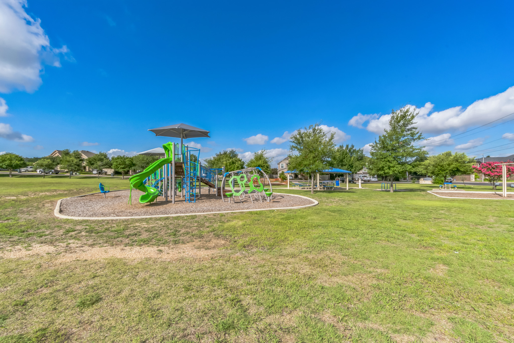 77 Jan Lane Georgetown, TX 78626 - Photo 3 of 16 A vibrant neighborhood park with a modern playground and mature trees under a clear blue sky.