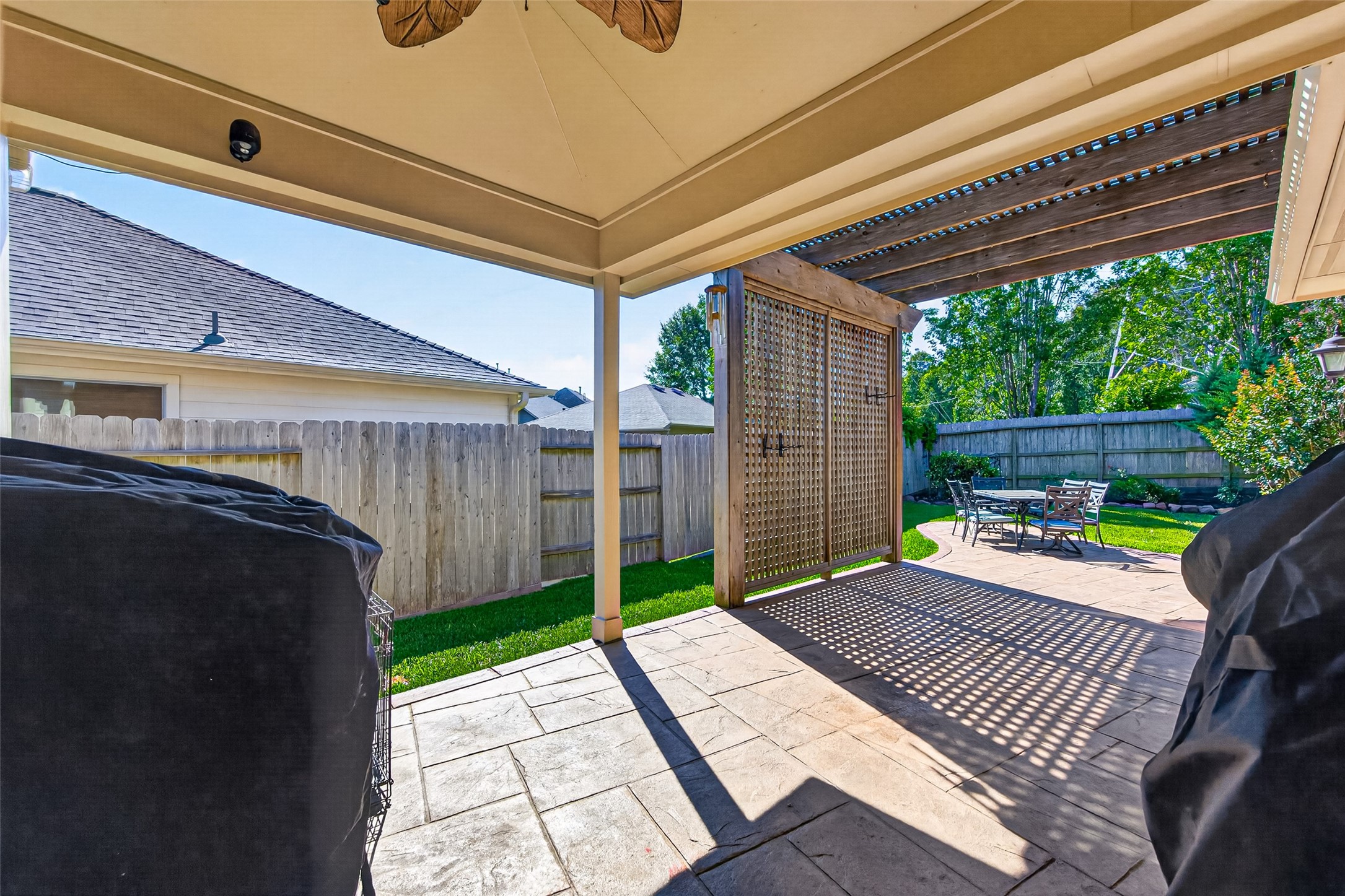 27443 Rebecca Field Lane Spring, TX 77386 - Photo 30 of 31 This photo showcases a covered patio area with a ceiling fan, adjacent to an open-air section with a pergola. The space features a paved surface, a privacy fence, and a cozy outdoor dining set, ideal for relaxation and entertaining in a sunny backyard.