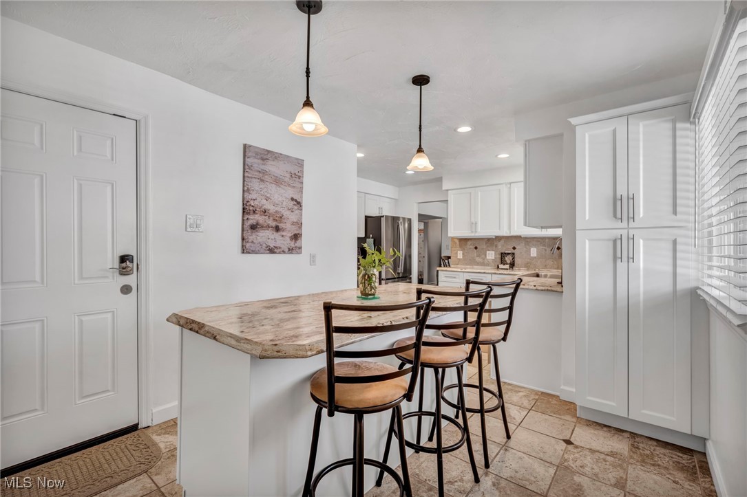 475 Harris Road Cleveland, OH 44143 - Photo 20 of 38 Kitchen with a kitchen island, freestanding refrigerator, light countertops, white cabinetry, and tasteful backsplash