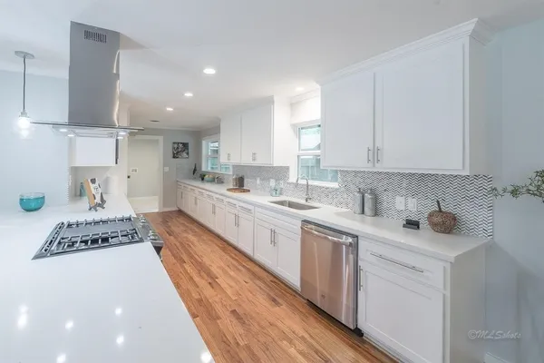 a large white kitchen with stainless steel appliances granite countertop a stove a sink a refrigerator and white cabinets