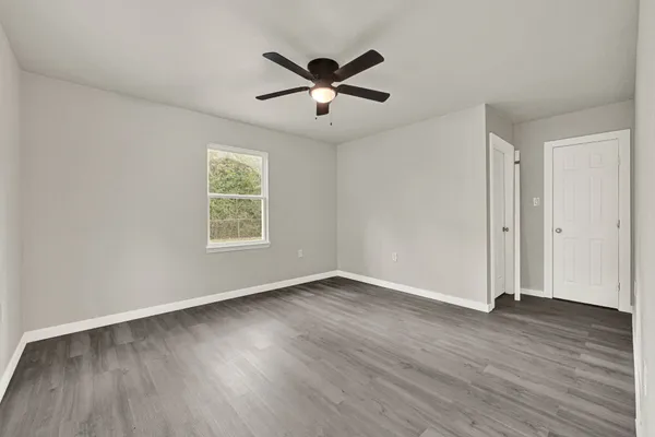 an empty room with wooden floor a ceiling fan and windows